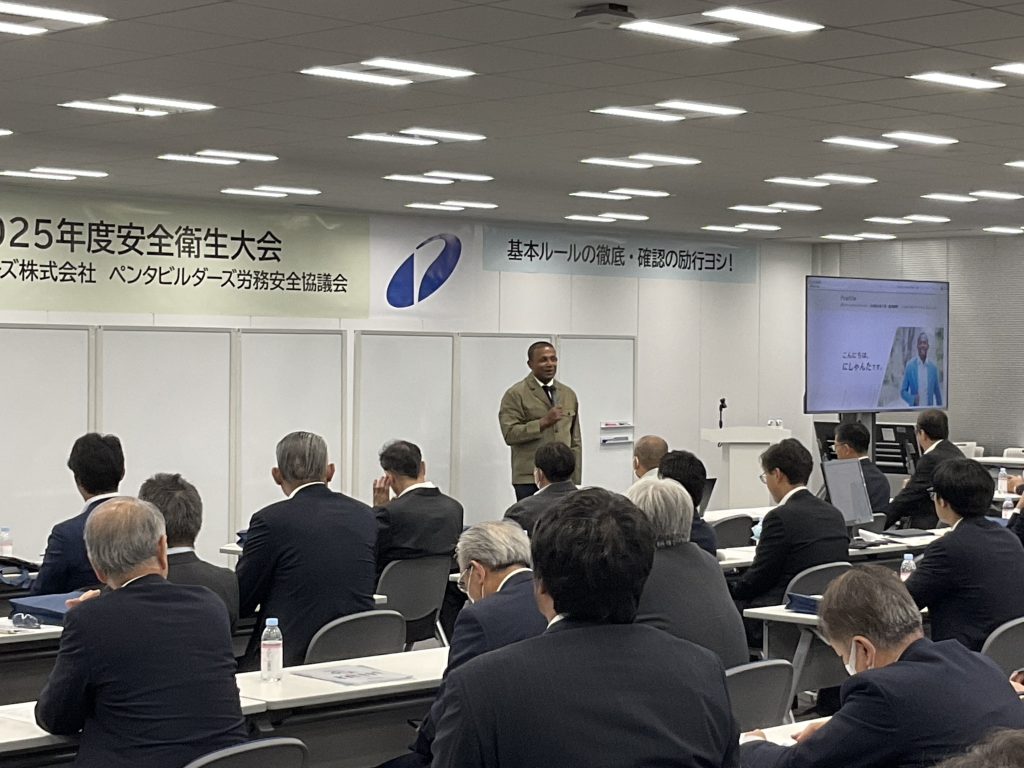 「伝わる安全」のポイントをスライドを用いて解説するにしゃんたの講演写真。外国人労働者の安全データやコミュニケーションの型を説明している場面。