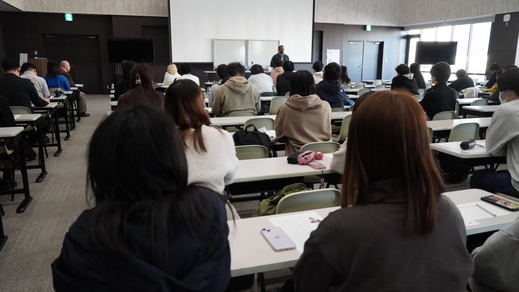 SDGsやダイバーシティ経営の視点も含めて解説を行うにしゃんたの講演スライドと様子