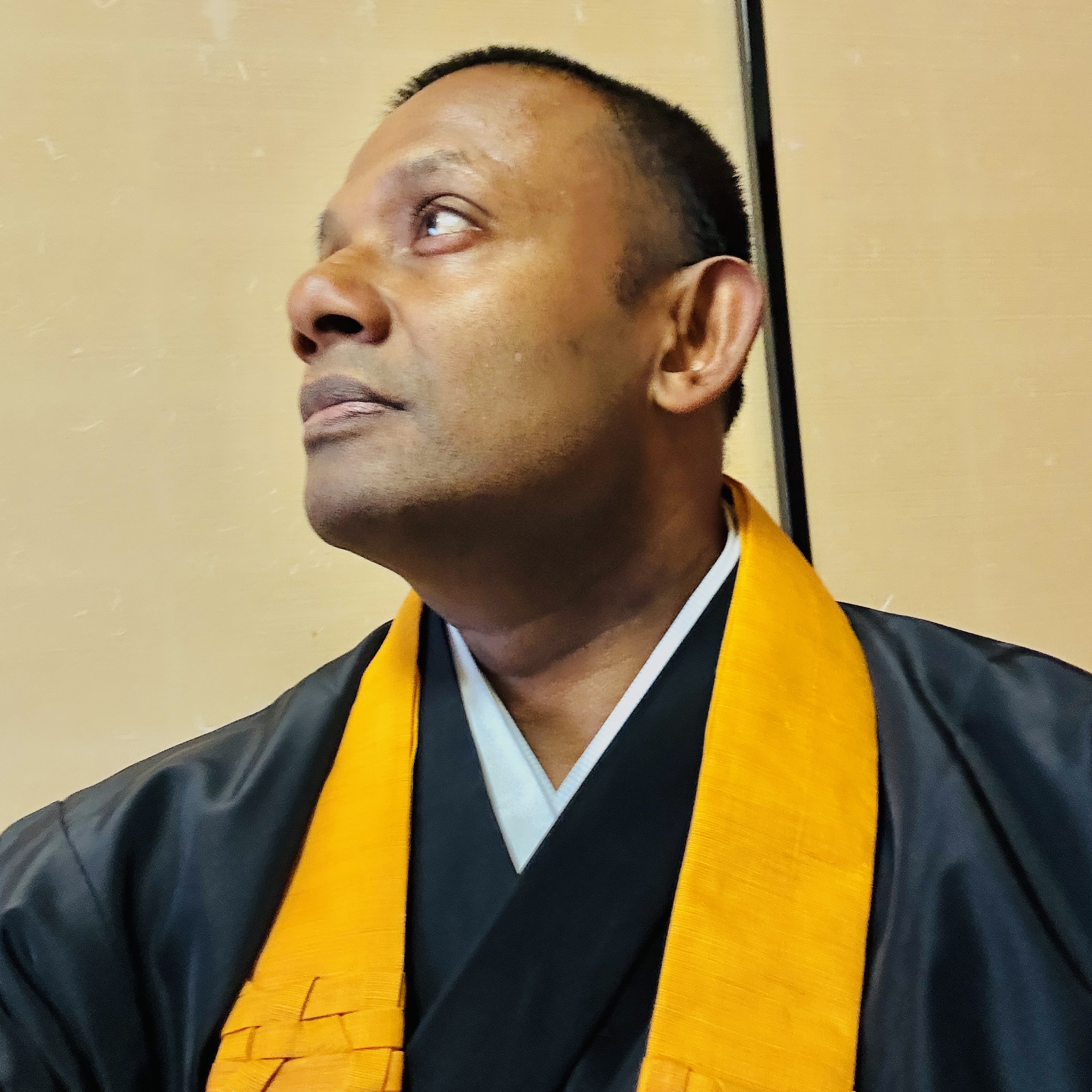 浄土真宗の僧侶として法衣をまとい、真剣な眼差しで遠くを見つめるにしゃんた